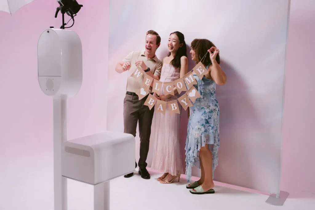 Group posing at the AIRi open-air photo booth with a soft pink backdrop